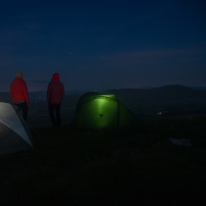 Ed and Chris stand still in the dark next to their tents. Each tent glows slightly from within.