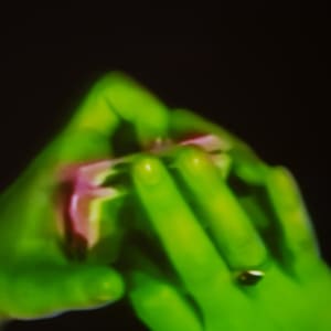 A video still of two hands manipulating a deck of cards. The hands are a luminous green, and the cards are a pink / magenta colour.