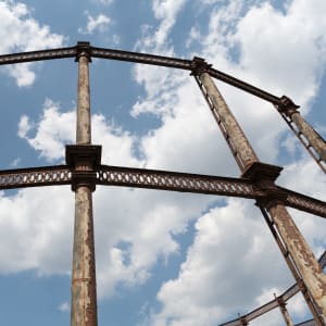 Looking straight up at the side of a gas works from close by. The metal railings are rusted with peeling paint.