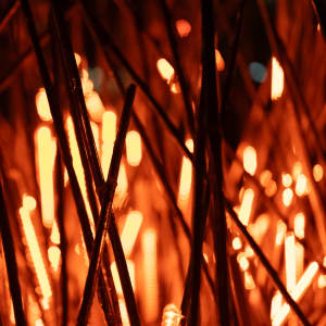 A close crop of a lighting installation made from thousands of short light sticks. Each light stick rhythmically glows orange. In the close crop, some sticks are unlit and the overall image has the appearance of fire.