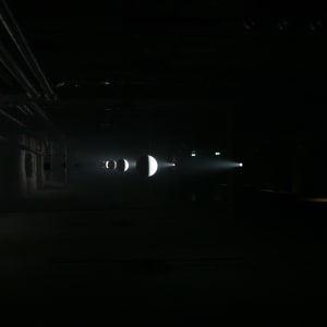 A pitch black room. A series of small white spheres are in the centre in a line to the distance. They are faintly light from the right casting shadows on the left wall. The White spheres look like moons.