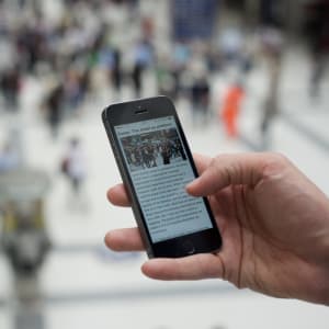 Photo of a hand holding a smartphone, which is showing a web article.
