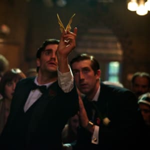 A man holding an origami paper bird, followed by other people.