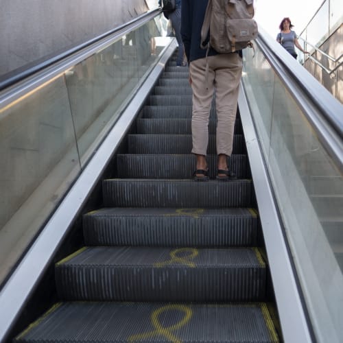 Photo looking up an escalator in to a bright sunny day. There’s someone on the escalator ahead.