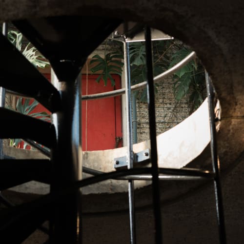 Looking up a spiral staircase at the level above. There’s a red door in the distance.