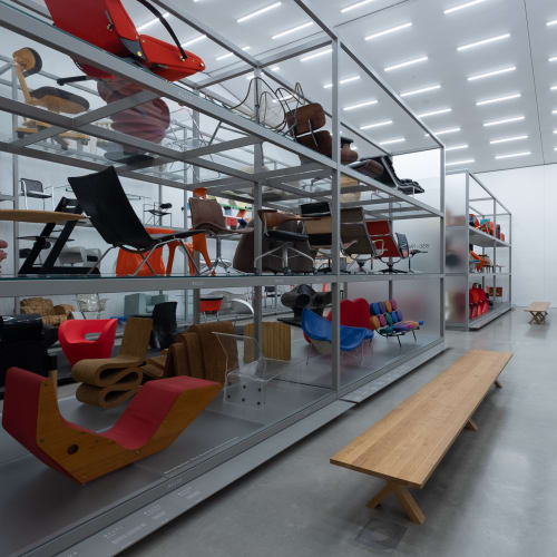 Inside the Vitra Design Museum archive. The room is brightly lit with aluminium shelves on each side receding in to the distance. On the shelves are many different chairs.
