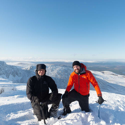 Ed and Chris kneel down with ice axes in hand at the top of Stob Coire an t-Sneachda