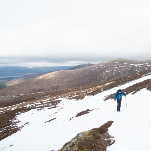 Ed hiking uphill on a partially snow covered slope.