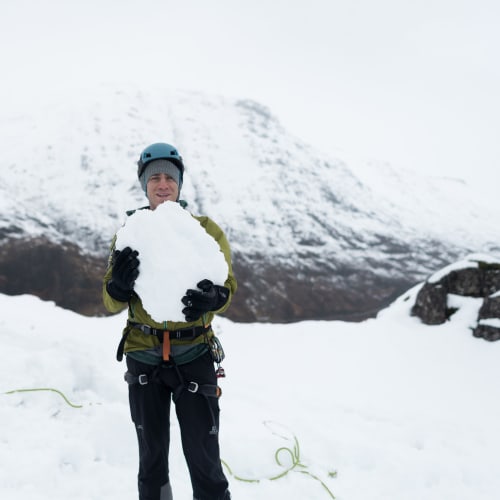Chris holds a large boulder of snow as he faces the camera.