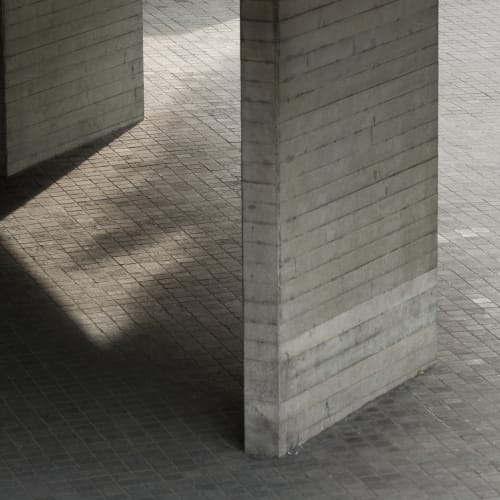 Looking down on two concrete supports for the first floor terrace of the National Theatre. The floor is tiled and the photo is otherwise very grey.