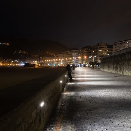 At night time, looking down the beach promenade to the city. There’s a mix of yellow sodium lamps with more modern white leds.