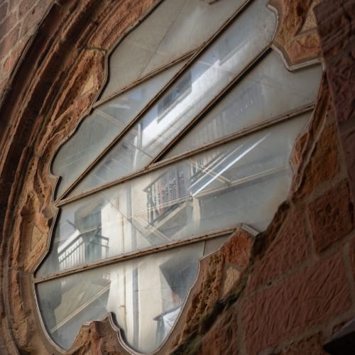 Looking up at the exterior of a church window. The surround is made from brown bricks, and you can see the neighbouring building reflected in the window glass.