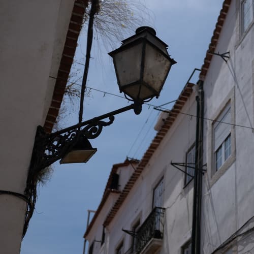 Looking up at a streetlamp in a narrow street. It’s daylight, so the streetlamp isn’t on.