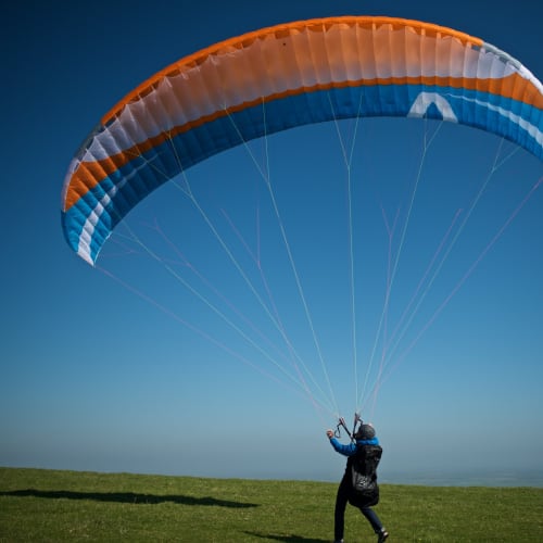 A paraglider stands on the ground with a large sail inflated overhead.