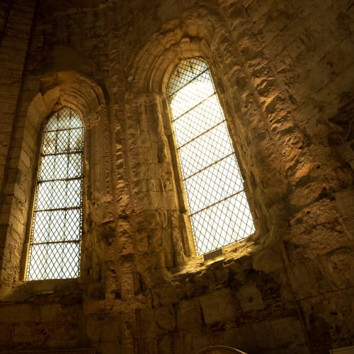 An interior view of three windows in the Carmo Convent - the interior is dark but warmly lit by the three windows.