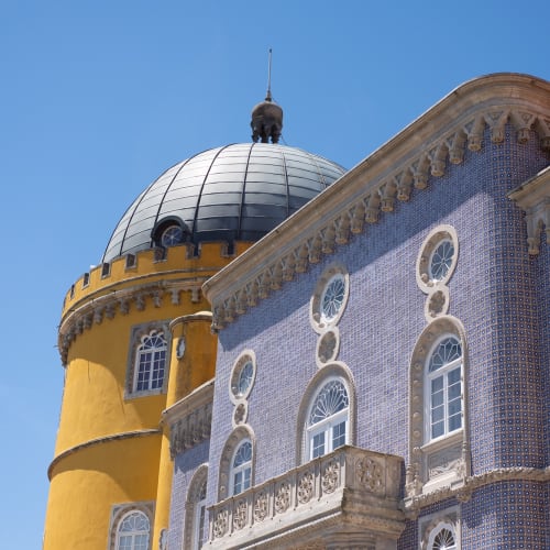 A view of two buildings in the Pena palace. the near building is covered in deep blue tiles with light stone trim. The far building is cylindrical and yellow.