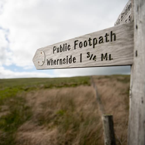 A footpath sign points from right to left, marking the summit of Whernside, 1.75 miles away.
