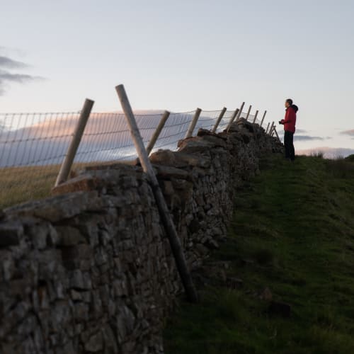 A stone wall recedes up and in to the distance. Chris stands at the far end looking out over one side.