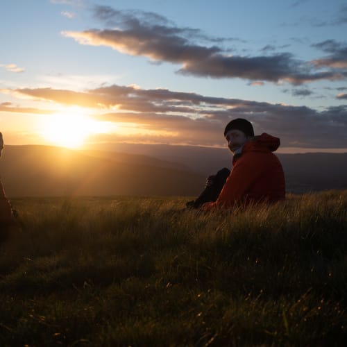 Ed and Chris sit on long grass in late golden sunset.