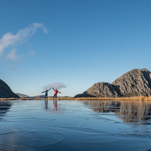 Ed and Chris pose on the other side of a small pond with arms outstretched. The pond is frozen with crystals extending over the surface.