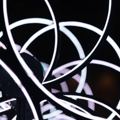 A close crop of of a lighting installation formed from many rings stacked in front of each other, with the inside of the ring light up in solid white. Seen from the front you can see many partial solid arks of white in a geometric pattern.