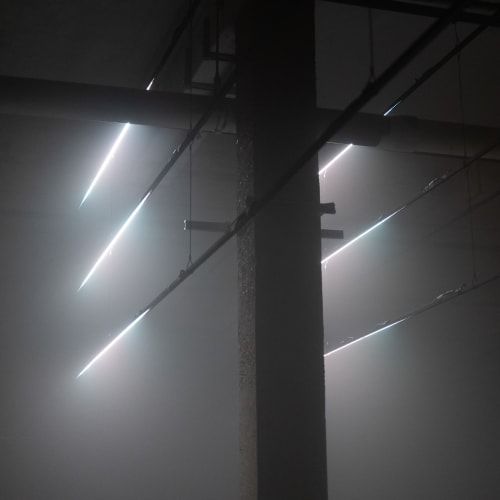 A dark scene with a single concrete pillar in the middle left. Six lines of light are evenly spaced vertically either side of the pillar. There’s fog in the room. Cables extend to and from the lines of light - reminiscent of telegraph poles.
