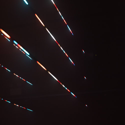 Multicoloured lines of light in a dark room converge to the bottom right.