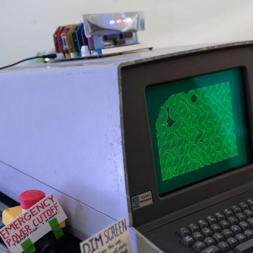 A vintage computer with glowing green display shows a pattern on screen.