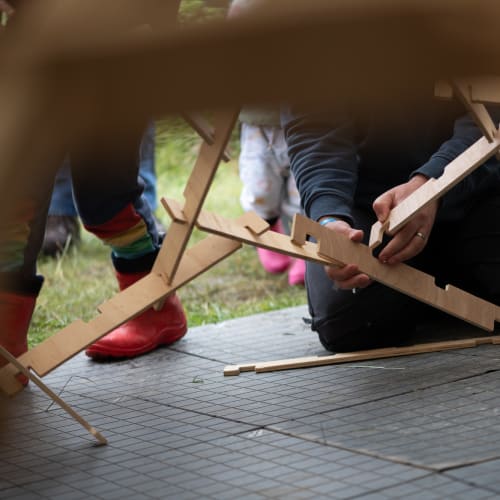 A person kneels down to connect two wooden slats of a large dome together