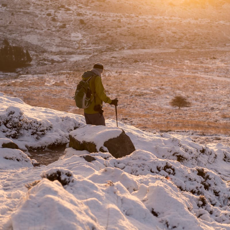 A hiker with hiking pole descends a snow covered hill at sunset.