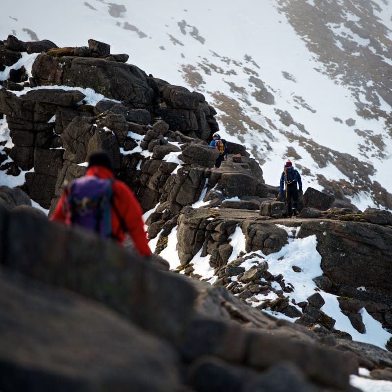 A photo taken facing along Fiacaill ridge. There’s climbers walking along various sections of it, with one in the foreground.