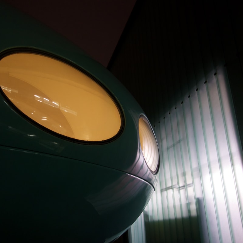 A detail of the exterior of Futuro house.  There’s two oval windows emanating yellow light, and white light on a building near the house.