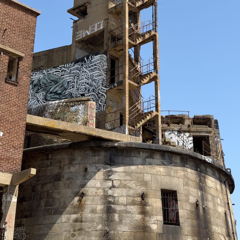 Exterior photo looking up a decaying concrete staircase attached to a narrow tower.