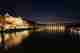 A panorama taken from a bridge over the Rhine at nighttime. There are buildings in the distance lit up and lights reflected in the water.