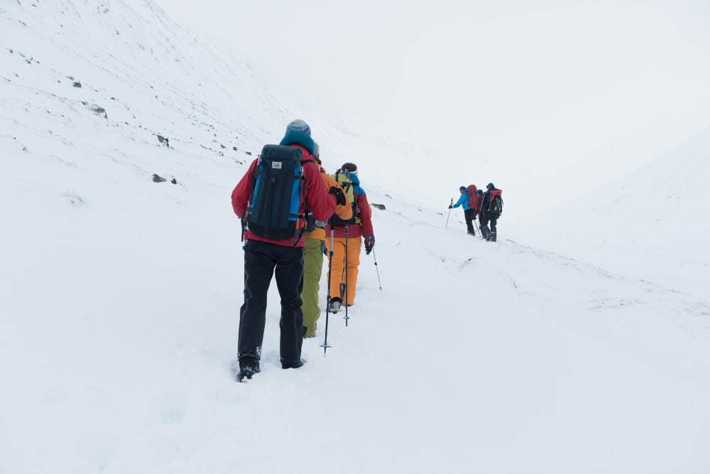 Two groups of climbers walk towards the horizon in snow. The sky is foggy / overcast and blending in with the ground. The climbers are all wearing brightly coloured clothing.