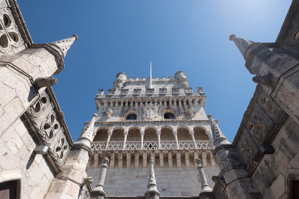 Wide angle photo looking up from the central courtyard at the Torre de Belém. The walls of the courtyard loom on each side, with the main tower in front. The sky is bright blue with no clouds.