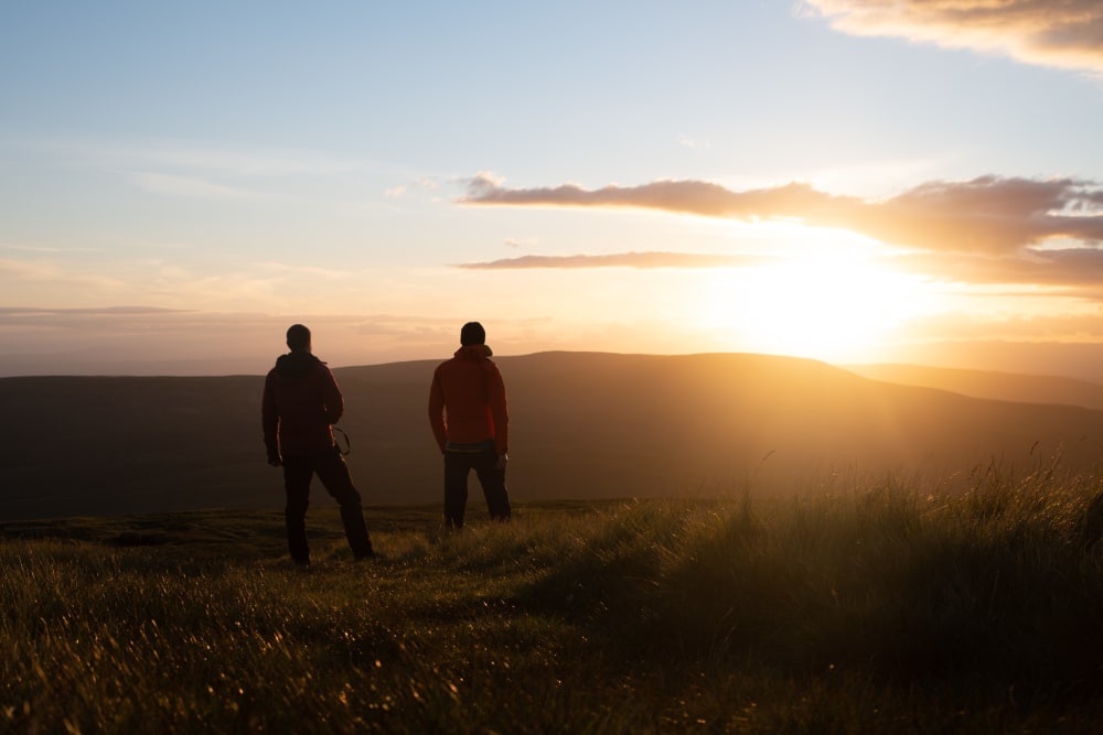 Ed and Chris stand in silhouette towards a very right and golden sunset.