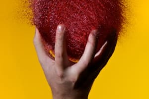 Photo of a burst water balloon. It’s dark red, and held in a hand.