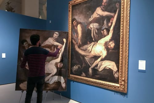 An artist painting a replica of a large oil painting hung on the wall.