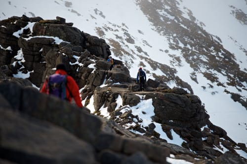 A photo taken facing along Fiacaill ridge. There’s climbers walking along various sections of it, with one in the foreground.