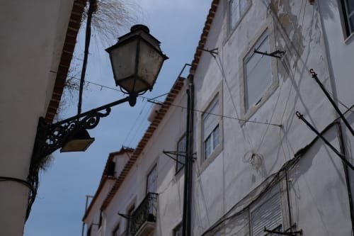 Looking up at a streetlamp in a narrow street. It’s daylight, so the streetlamp isn’t on.