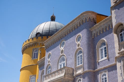 A view of two buildings in the Pena palace. the near building is covered in deep blue tiles with light stone trim. The far building is cylindrical and yellow.