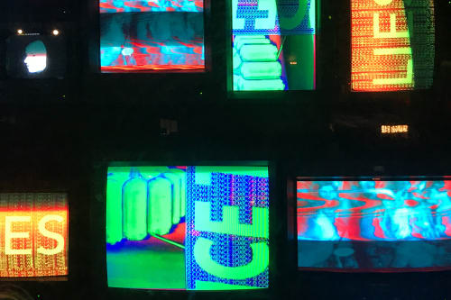 Several vintage TVs stacked together display abstract brightly coloured slogans.