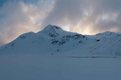 A panorama taken from the bowl of the Ring of Steall at dusk. The sky is still bright with dramatic clouds, but the mountains and ground around are getting dark.