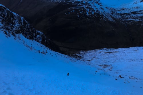 Chris a way ahead descending a snowy mountain after dusk.