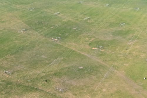 Drone photo looking over a empty large grass field filled with football pitches.