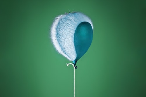 Photo of a water balloon bursting; it is attached to a string like a helium balloon.