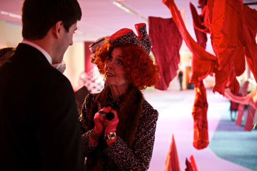 A woman wearing a shoe-hat talks to a man.