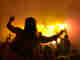 A music fan sits on a friend’s shoulders and sways in the yellow smoky light in front of the stage.