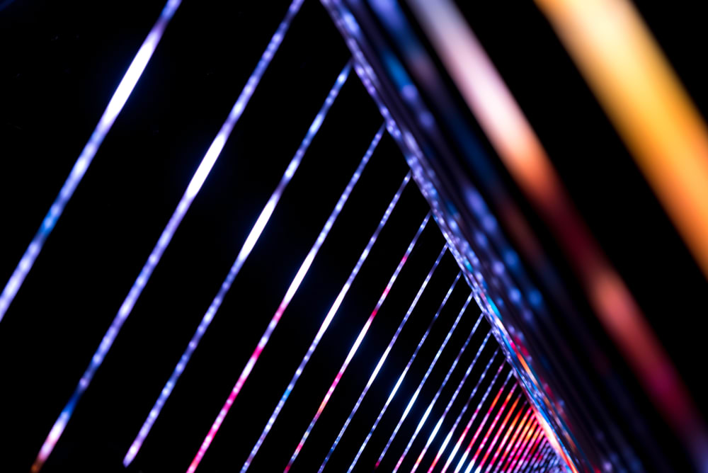 A photo of a light triangular light sculpture. A series of triangles is each lit up in white and bright colours. The triangles recede in to the distance.